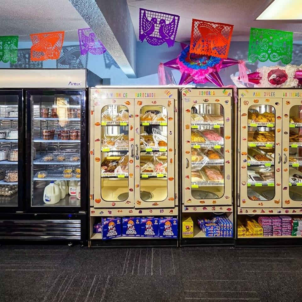 Refrigerated cases filled with Mexican pan dulce, cakes, and groceries, decorated with colorful papel picado.