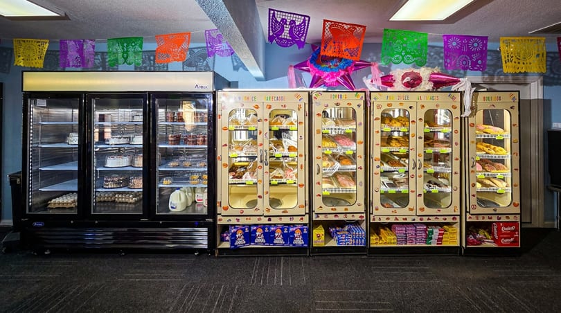 Refrigerated cases filled with Mexican pan dulce, cakes, and groceries, decorated with colorful papel picado.
